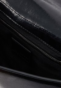 Černá kabelka s lesklou texturou, kapsou na zip a látkovou podšívkou. Obsahuje nenápadnou vnitřní cedulku na černé látce.