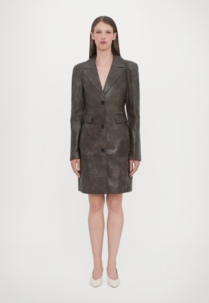 Abito blazer in pelle marrone con una vestibilità sartoriale, colletto elegante, tre bottoni e tasche laterali, che termina sopra il ginocchio. Texture liscia.