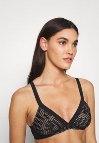Bralette negra con un diseño triangular, patrón texturizado, tirantes anchos y banda elástica. Material ligero con acentos de malla transpirable.