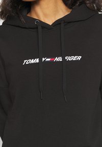 Felpa nera in cotone con logo frontale che riporta "TOMMY HILFIGER" in bianco, con accenti di strisce rosse e blu, dotata di cordini regolabili.