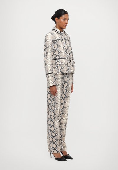 Conjunto de traje a medida en estampado de serpiente beige y negro, que incluye una chaqueta corta con solapas y pantalones de pierna recta, combinados con tacones negros.