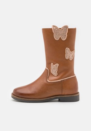 Botte en cuir marron montant jusqu'au milieu du mollet avec trois patchs papillon scintillants et une semelle basse noire sur fond blanc.