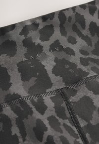 Zwarte legging in sportkledingstijl met een grijs luipaardprintpatroon, met een gladde, rekbare textuur en gestikte naden. De merknaam is zichtbaar.