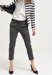 Pruhované sako v námořnické modři a bílé barvě, doplněné šedými úzkými kalhotami. Modré vysoké podpatky. Sako má zkrácený střih a otevřený přední díl.