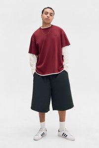 Rød t-skjorte med korte ermer lagdelt over en hvit langermet skjorte, svarte shorts og hvite sneakers med svarte striper. Enkelt design, avslappet passform.