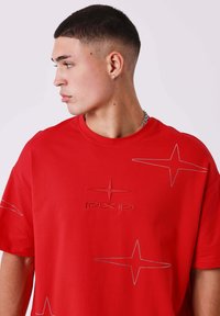 Rood T-shirt met korte mouwen, voorzien van een geborduurd "PXP" logo en stermotieven in contrasterende draad. Zacht katoenmateriaal, losse pasvorm.
