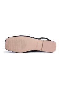 Black sandal with a flat sole, featuring a smooth texture and subtle ridges for grip. Minimalist design, with thin straps crossing over the foot.