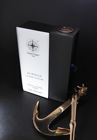 Home fragrance doos in het zwart met een wit etiket met gouden tekst. Inclusief een gouden haakvormig accent, onderdeel van de Winds Collectie.