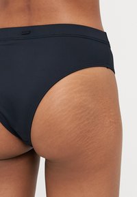 Black swim bikini bottom with smooth, stretchy material. Features a low-rise design and stitching details along the waistband.