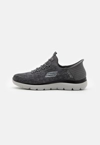 Zapatilla deportiva gris con parte superior texturizada, acentos negros, cordones elásticos y una gruesa suela blanca, diseñada para la comodidad y la flexibilidad.