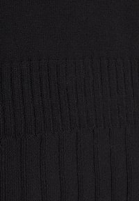 Gros plan sur un tissu noir tricoté avec une texture côtelée montrant des lignes verticales et des points serrés.