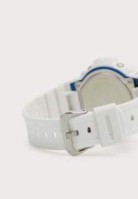Bracelet de montre en silicone blanc avec boucle en métal argenté, trous découpés pour le réglage et accents bleus sur le boîtier de la montre.