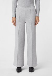 Graue weit geschnittene Hose aus weichem Material mit glatter Textur, ausgestattet mit vorderen Falten und einem hohen Bund. Schwarze Schuhe ergänzen das Outfit.