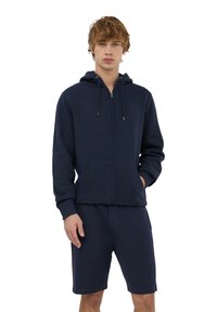 Nawigacyjny hoodie na zamek błyskawiczny z kapturem na sznurki i kieszeniami z przodu, zestawiony z dopasowanymi szortami w kolorze navy, wykonanymi z miękkiego, teksturowanego materiału.