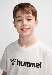Hvid bomulds T-shirt med et stort sort "hummel" logo på brystet. T-shirten har rund hals og korte ærmer.
