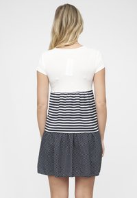 Haut blanc à manches courtes avec corsage rayé bleu et blanc ; jupe noire à pois avec détail froncé. Tissu lisse, design décontracté.