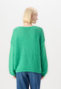Grøn strikket oversized sweater med et struktureret mønster, brede ærmer og en rund halsudskæring, parret med blå denim jeans.