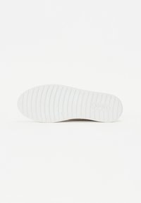 Semelle de chaussure en caoutchouc blanc avec une surface textur ée à rainures et un logo circulaire. Design minimaliste, sans motifs ni accents visibles.