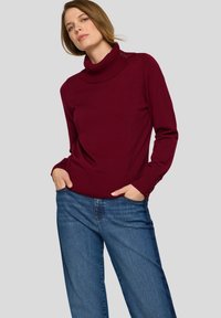 Weinroter Rollkragenpullover mit geripptem Kragen und Knopfdetails an den Schultern, kombiniert mit hellblauen Jeans mit weitem Bein. Glatte Textur.