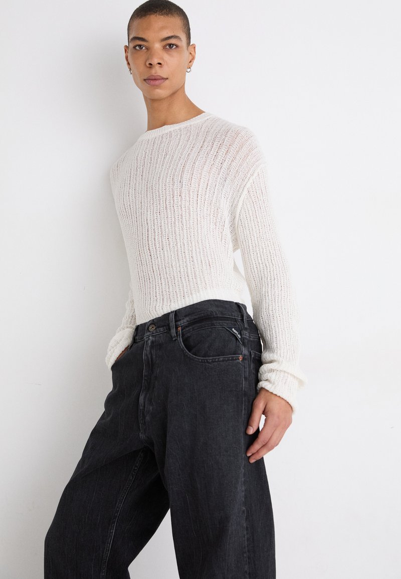 Cremfarbener Rippstrickpullover mit langen Ärmeln, kombiniert mit schwarzen, übergroßen Denim-Jeans mit einer Vordertasche und dezenten Stickdetails.