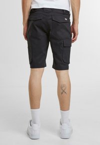 Pantaloni cargo neri caratterizzati da numerose tasche utilitarie, dettagli cuciti e una vestibilità comoda. Indossati con sneakers bianche e calzini alla caviglia.