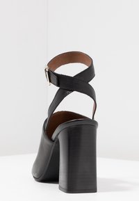 Černá vysoká elegantní bota na podpatku s masivním podpatkem, designem s křížovým páskem a hladkou koženou úpravou. Vnitřek je podšitý hnědou látkou.