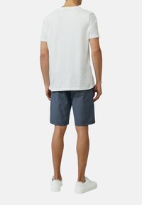 Weißes Baumwoll-T-Shirt mit kurzen Ärmeln, kombiniert mit navyblauen gestreiften Shorts und weißen Sneakers. Fokus auf lässigem, entspanntem Schnitt.