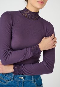 Maglia viola a maniche lunghe con colletto in pizzo alto e bordo in pizzo ai polsini, caratterizzata da una texture a costine e un design aderente.