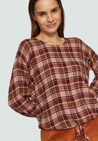 Haut à manches longues en tartan dans des tons de rouge, rose et marron avec une coupe ample et un cordon de serrage à l'ourlet, fabriqué en tissu léger.