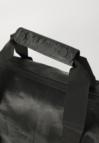 Black waterproof bag with textured surface, featuring a sturdy handle, black snaps, and durable strap accents. Minimalist design.