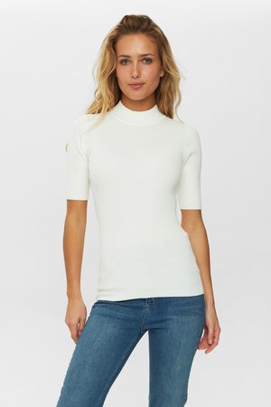 Geribbelde witte top met korte mouwen en een hoge hals, vouwsluiting en gladde textuur, gecombineerd met blauwe jeans.