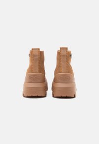 Tan gležnjači s mekim nubukom, debelim gumiranim podplatom, trakicom za povlačenje na stražnjem dijelu i utisnutim logom brenda na peti.