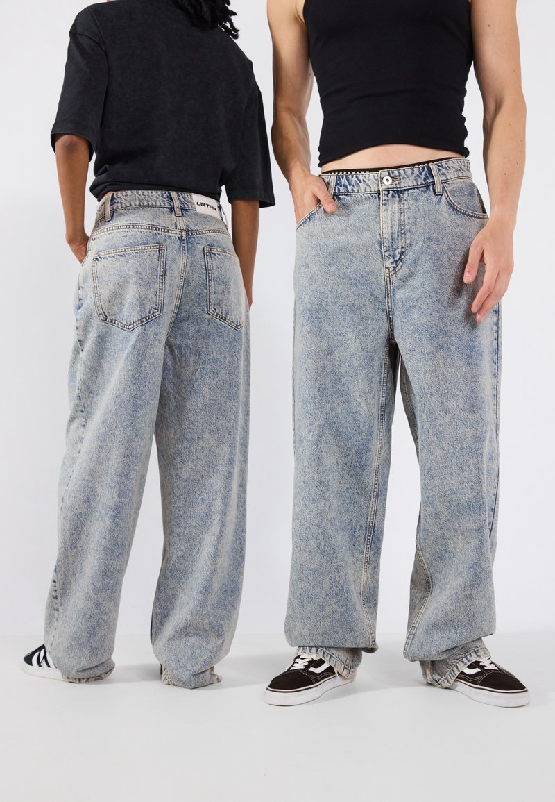 Jeans in denim azzurro chiaro con una vestibilità ampia, dotati di una vita alta, cinque tasche e orli sfilacciati. Abbinati a sneaker nere.