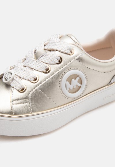 Χρυσό μεταλλικό αθλητικό παπούτσι με λευκά χοντρά κορδόνια, στρογγυλό λογότυπο Michael Kors στο πλάι και λευκή καουτσούκ σόλα.