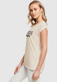 Beige, short-sleeve T-shirt made of soft cotton. Features bold black text on the front. Classic fit and simple rounded neckline.