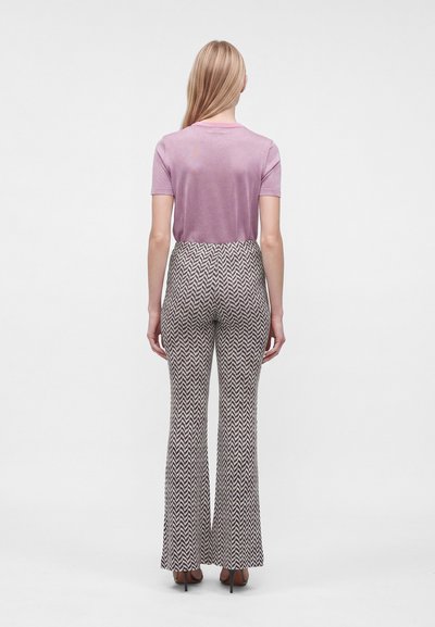 Femme vue de dos portant un haut rose à manches courtes et un pantalon taille haute à motif chevron avec des talons noirs.
