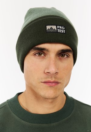 Beanie hat in dark green ribbed knit with a light green band and a rectangular logo patch that reads "PRO TEST." Soft texture.