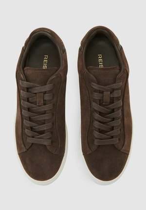 Bruine suède sneakers met platte veters, een ronde neus en een witte rubberen zool. Het interieur heeft een ingegraveerde merknaam in goud.