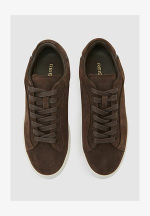 Bruine suède sneakers met platte veters, een ronde neus en een witte rubberen zool. Het interieur heeft een ingegraveerde merknaam in goud.