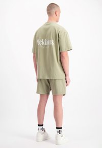 Olijfgroen katoenen tweedelige outfit met een losse t-shirt met witte branding op de rug en bijpassende shorts.