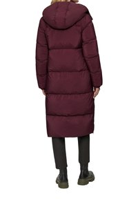 Bordeaux pufferjack met een capuchon, met een knielange design, horizontaal geweven patroon en elastische manchetten. Gecombineerd met donkere broeken en laarzen.