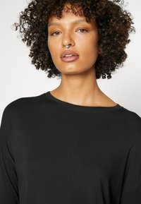Zwarte langwerpige shirt met een wijde halslijn en een relaxte pasvorm, gemaakt van een zachte stof. Heeft een gladde textuur en minimale stikdetails.