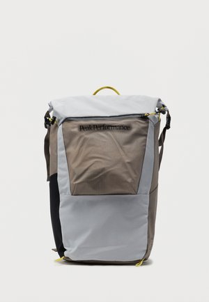 Sac à dos rectangulaire en gris et beige avec panneau latéral noir, fermeture éclair supérieure, languettes jaunes et logo "Peak Performance" sur la poche avant.
