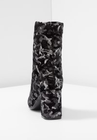 Bottine noire avec motif camouflage argenté, texture douce et talon carré. Le design présente une silhouette épurée et un bout arrondi.