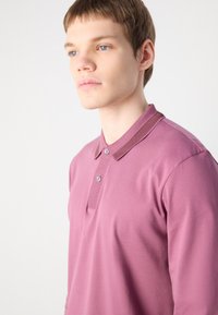 Polo de manga longa em mauve claro, com colarinho canelado, palas de dois botões e textura de tecido suave.