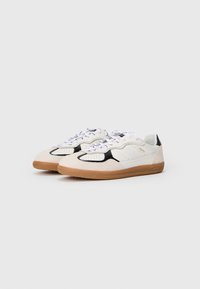 White and black sneakers with a textured suede upper, rubber gum sole, and white laces. Features perforated detailing on the toe box.