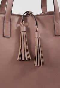 Sac à main en simili cuir marron avec deux accents de pompons assortis. Caractérisé par un design élégant et structuré avec des détails de couture contrastés.