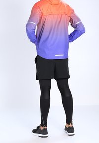 Chaqueta ligera con un degradado de naranja a púrpura, combinada con pantalones cortos negros y leggings negros ajustados, todo acentuado con detalles reflectantes.