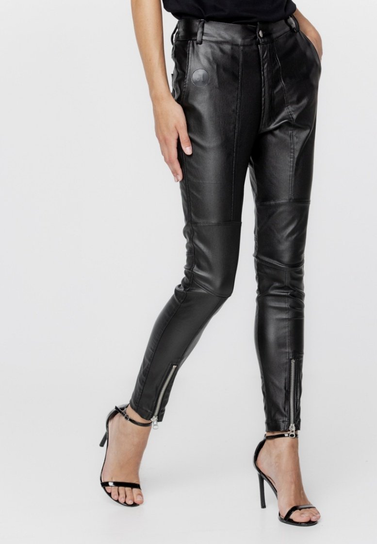 Czarne skórzane spodnie o dopasowanym kroju, z przednimi kieszeniami, detalami szwów oraz zamkami błyskawicznymi przy kostkach. Noszone z czarnymi sandałami na obcasie.