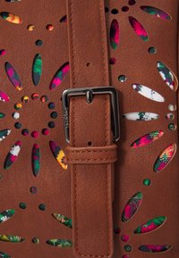 Brązowa torba z perforowanej ekoskóry z kwiatowym wnętrzem, w zestawie z dopasowanym paskiem i metalowym zapięciem.